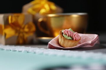 Single tiny sweet cake on blurred gold coffee cup and gift boxes background. Homemade things concept. Golden colour concept. Sustainable Christmas.