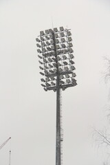 Stadium floodlight with metal pole, lighting mast, tower with floodlights in the sports stadium against the white sky.