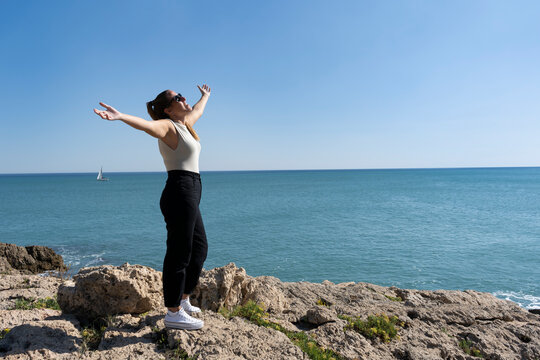 Beautiful young woman enjoying freedom with open arms standing on the rocks next to the sea.Lifestyle of happiness, success and freedom people concept.