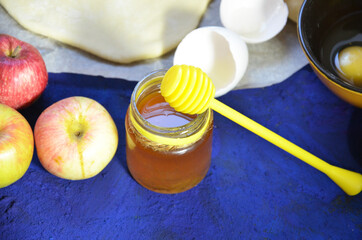 Various ingredients for winter seasonal baking and other recipes, honey, apples, herbs and spices on a dark blue background. Top view.