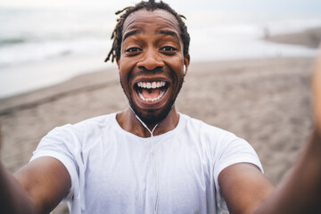 Cheerful black man with earphones standing on beach
