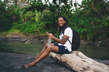 Optimistic black traveler browsing smartphone on riverbank © BullRun