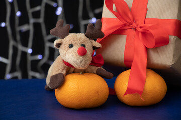 A gift wrapped in craft paper with a red wide ribbon stands on a blue table near the Christmas tree. Holidays.
