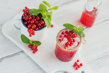 Summer drink with white sparkling wine. Homemade refreshing fruit cocktail or punch with champagne, red currant, ice cubes and mint leaves on white wooden background