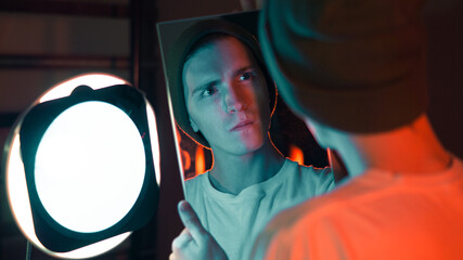 man frowning at his reflection in the mirror, studio photography, young guy, hipster indoors in a...