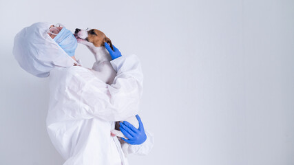 A woman in a protective suit and mask is holding a Jack Russell Terrier dog on a white background