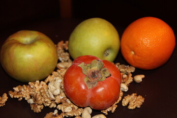 Green apples, persimmons and oranges on a background of scattered walnuts
