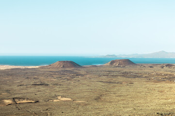 Landscape of volcanoes and ocean in Calderón Hondo (Fuerteventura, Canary Islands) with Lanzarote island in the background.