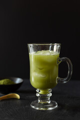 Green matcha iced tea in a long glass on black background.