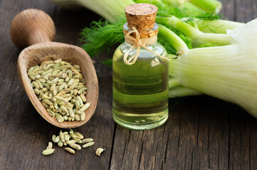 Glass bottle of fennel essential oil with fennel seeds and bulb on wooden table. Herbs alternative...
