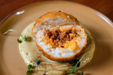 Sliced meat baked in rice with mashed potatoes, garnished with herbs on a clay plate close-up.