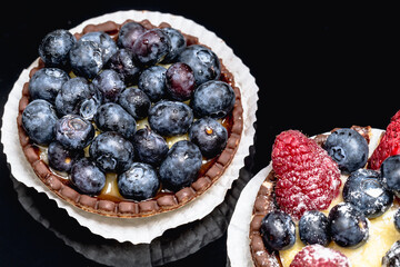 Tartelette mit Blaubeeren, Himbeeren und Erdbeeren vor einem schwarzem Hintergrund