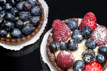 Tartelette mit Blaubeeren, Himbeeren und Erdbeeren vor einem schwarzem Hintergrund