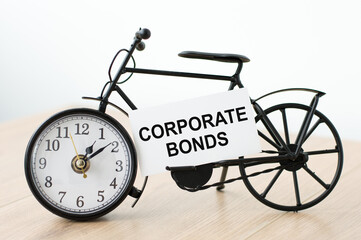 Card with text Corporate Bonds. On the table there is a clock in the shape of a bicycle with a card.