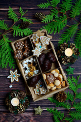 Christmas composition from a craft box with marshmallows, chocolate and cookies on a background of green spruce branches. Top view. Vertical