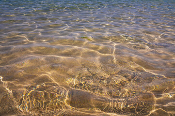 Distorted texture of sand under water. Transparent water ripples, sand waves and glare of sunlight. Seabed background