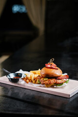 Juicy burger with fries on wooden board.