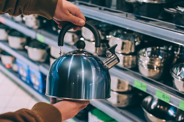 A man in a supermarket holds a metal kettle.
