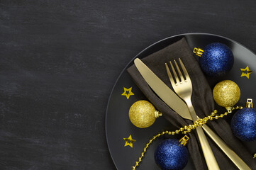Festive table setting with black plate, golden cutlery and xmas decorations on dark chalkboard....