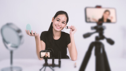 Asian teen woman sit in front of camera and live broadcasting as a beauty blogger influencer or youtuber to review or advice about how to make up at home. studio shot white background.