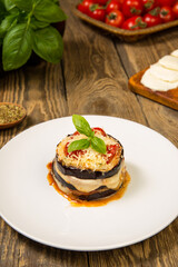 Baked eggplant and tomatoes mozzarella and parmesan stacks with ingredients on a rustic wooden table. Close up. Selected focus.