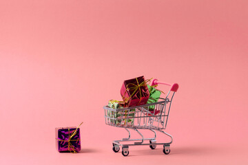 shopping trolley full of present boxes copy space, shopping concept poster on a pink background