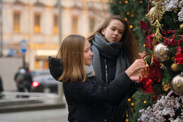 Fototapeta premium Two female best friends on Christmas Market. Adorable sisters having fun together on traditional Christmas fair. Winter time with family. Girls enjoying the scenery and atmosphere on Xmas market.