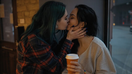 Lesbian young woman comes and hugs her partner with coffee cup in hands