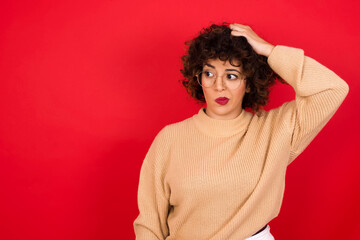Fototapeta na wymiar Young beautiful Arab woman wearing beige sweater against red background saying: Oops, what did I do? Holding hand on head with frightened and regret expression.