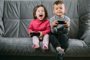Brother and sister with a gamepad in their hands playing games shouting having fun