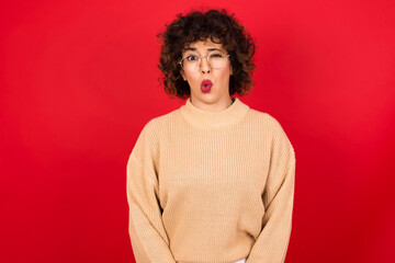Obraz na płótnie Canvas Young beautiful Arab woman wearing beige sweater against red background expressing disgust, unwillingness, disregard having tensive look frowning face, looking indignant with something.