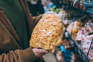 A man in a supermarket holds a bag of cereals.