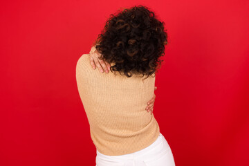 Young beautiful Arab woman wearing beige sweater against red background hugging oneself happy and...