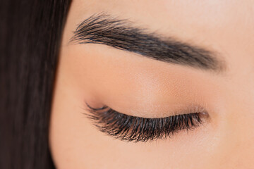 Eyelash extension procedure. Beautiful female asian eyes with long lashes closeup