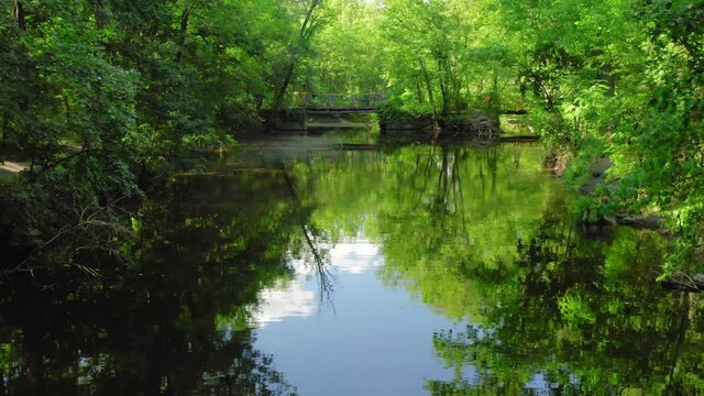 Slowly flying over beautiful river between banks covered with green trees, drone moving forward