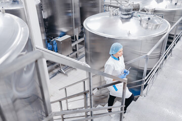 Worker female operator in uniform holding computer tablet checking food factory production line and...