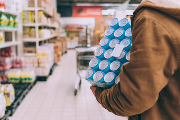 A shopper in a supermarket holds a package of beer in his hands.