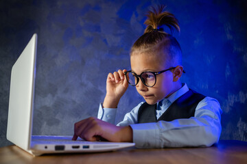 Young businessman at work in office. Modern child in glasses. Little boy is working on laptop.