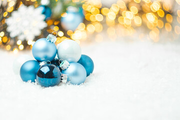 Blue Christmas balls laying on the snow on the background of Christmas tree and blurred golden...