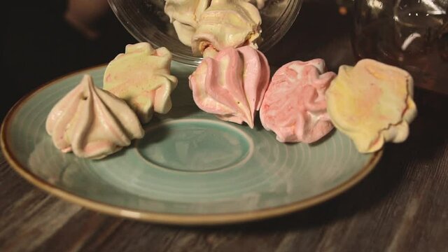 Multicolored meringue pour out from paper bag to plate. Sweets for tea. Slow motion footage