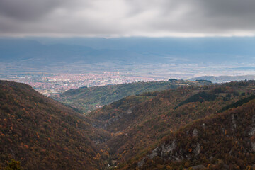 Dark, moody, murky sky above distant Pirot city, foreground canyon and autumn, golden colored trees