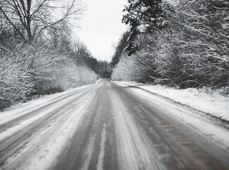 snowy road surrounded by pine trees, driving in winter snow on a country road, selective focus and...