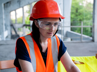 Smiling charismatic lady engineer in orange hard hat looking at laptop at construction site