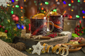Mulled wine with orange slice, cinnamon stick on the background of festive garland lights. Dark style