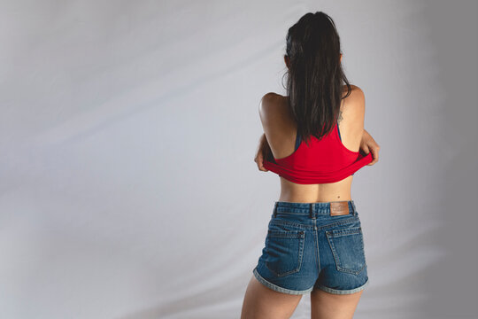Mujer j&oacute;ven de espaldas quit&aacute;ndose un top rojo