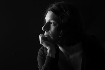 low key portrait of serious woman with hand on chin and thinking on black background