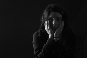 pensive woman with both hands on her face looking at camera on black background