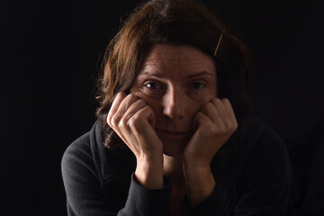 ensive woman with both hands on her face looking at camera on black background