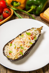Eggplant stuffed with vegetables baked with parmesan and ingredients on a rustic wooden table. Close up. Selected focus.