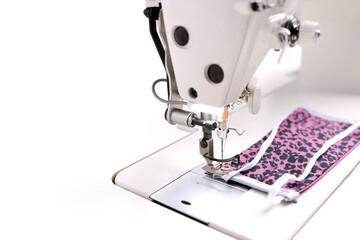 An individual pink protective cotton face mask with screen print is produced with an industrial high-speed sewing machine in bright light - sustainable pandemic fashion concept